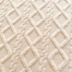 Cette image montre un gros plan d'un motif texturé de tissu moelleux de couleur beige clair, composé de motifs géométriques entrelacés.