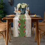 Une table rustique en bois avec un chemin de table en toile de jute décoré de brindilles de pins et de baies rouges, entourée de verres à vin et de fruits, créant une scène chaleureuse et festive.