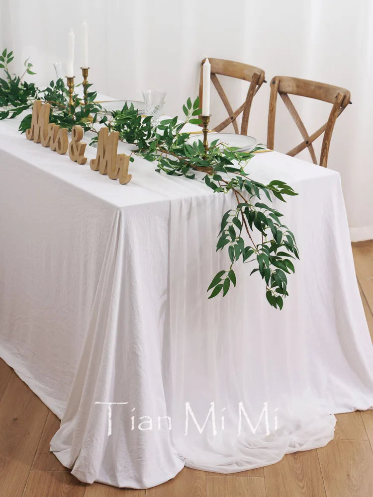 Cette image montre une table de mariage décorée avec des chandelles, des plantes vertes et un tissu blanc avec les mots "Tian Mi Mi" écrits dessus. L'ensemble de la décoration crée une atmosphère chaleureuse et élégante.