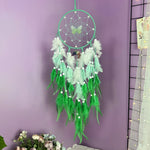Un magnifique attrape-rêves vert et blanc aux formes élégantes, avec des plumes et des perles qui s'entremêlent dans un motif sophistiqué, suspendu au mur comme une œuvre d'art décorative.