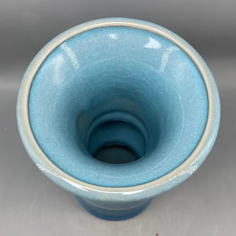 Le vase présente une forme cylindrique et une surface vitrifiée bleutée, créant un effet visuel intéressant et apaisant.