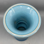 Le vase présente une forme cylindrique et une surface vitrifiée bleutée, créant un effet visuel intéressant et apaisant.