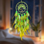 Un capteur de rêves fait main et décoratif, constitué d'un anneau noir avec un arbre de vie verdoyant représenté au centre, entouré de plumes jaunes et vertes.