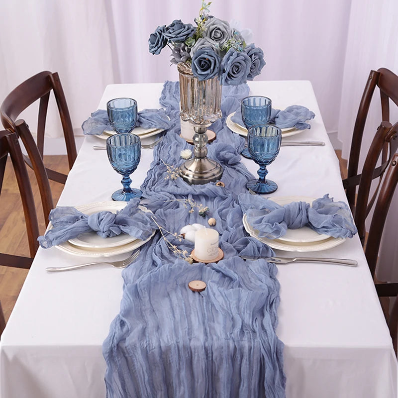 Cette table de salle à manger est élégamment décorée avec un bouquet de roses bleu-gris, des verres assortis, une nappe texturée et d'autres accessoires décoratifs, créant une atmosphère chic et raffinée.