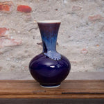 Vase en céramique de couleur pourpre profond avec des motifs bleutés, posé sur une surface en bois.