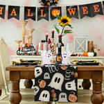 Une table de fête décorée pour Halloween avec des fantômes, des citrouilles et des bougies sur un fond de bannière festive.
