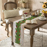 Une table de salle à manger en bois rustique avec un chemin de table de Noël orné de branches de sapin et de baies rouges, accompagnée d'un fauteuil en rotin et d'une décoration florale.