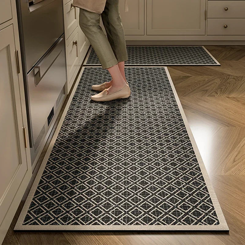 Le sol de la cuisine est recouvert d'un tapis de couleur noire et blanche avec un motif géométrique, sur lequel une personne porte des chaussures plates.