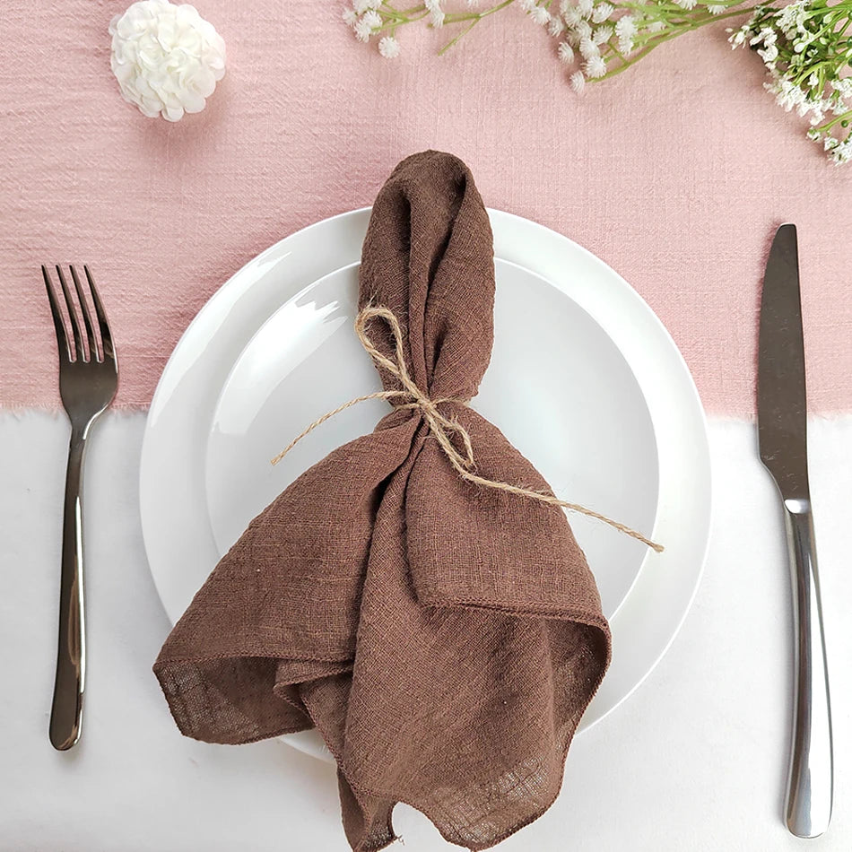 Une belle table dressée avec des fleurs blanches et une serviette de table brun foncé pliée et attachée avec de la ficelle.