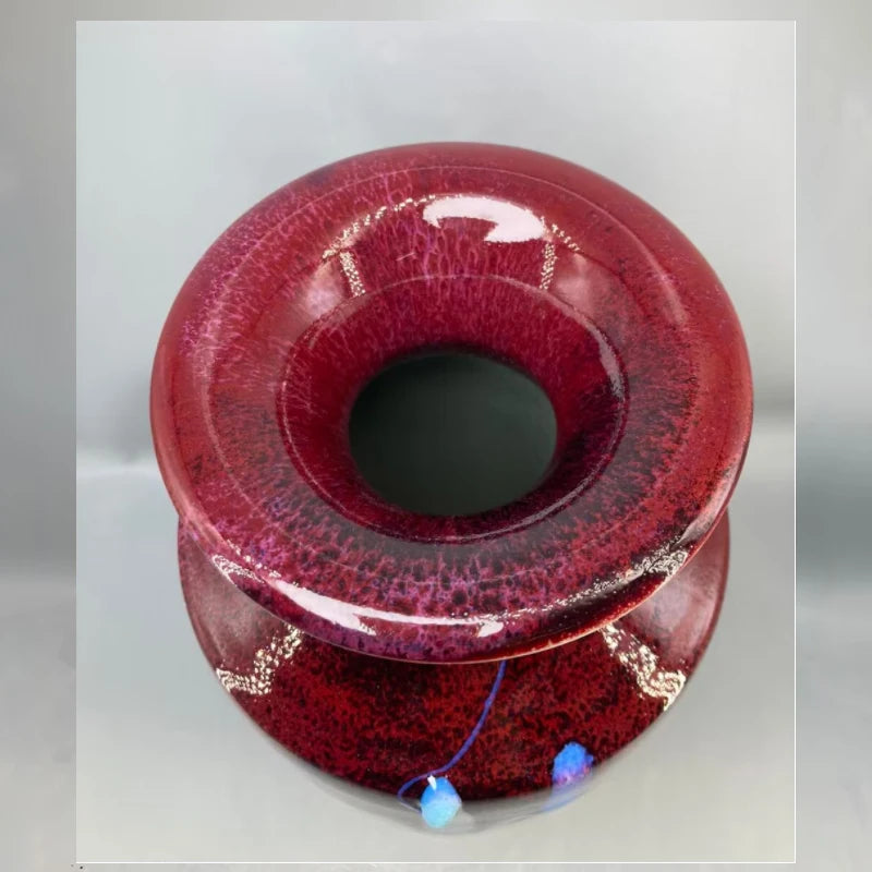 Vase en verre de forme ronde et teinte rouge foncé, avec une surface texturée et brillante, et des éléments décoratifs bleu pâle incrustés dans le verre.