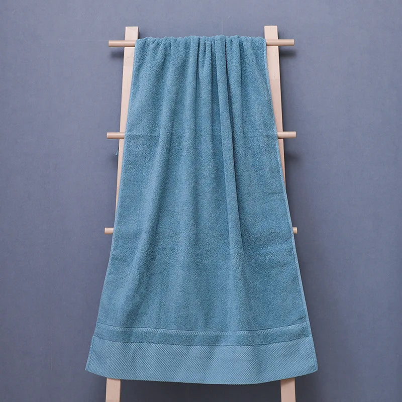 Une serviette de bain bleue suspendue sur un portant en bois contre un mur gris.