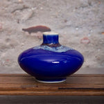Un magnifique vase en céramique bleu foncé avec des motifs texturés, posé sur une surface en bois rustique.