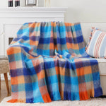 Couverture douillette et colorée en laine avec des motifs géométriques bleus, orangés et gris, parfaite pour se réchauffer confortablement sur un canapé ou un lit.