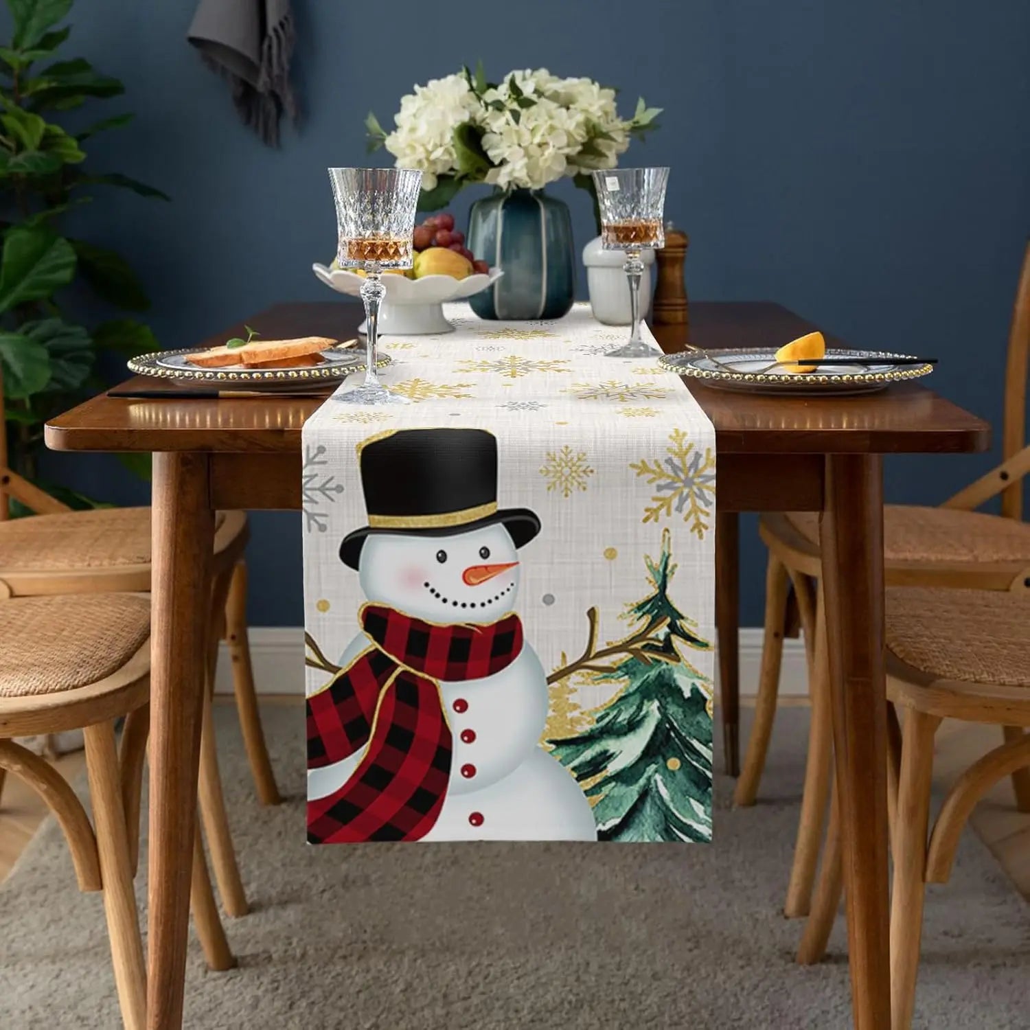 Une belle décoration de table hivernale avec un chemin de table orné d'un adorable bonhomme de neige, de flocons de neige et d'un sapin de Noël, accompagnés de fleurs fraîches et de verres à vin.