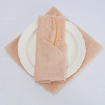 Une serviette beige en lin avec un motif de plume décorative est posée sur une assiette blanche.