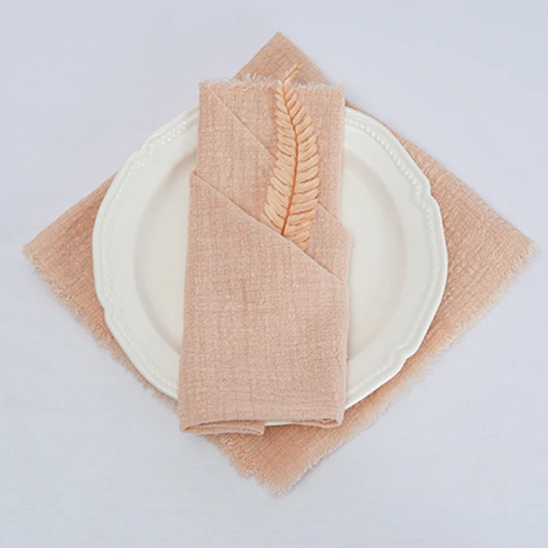 Une serviette beige en lin avec un motif de plume décorative est posée sur une assiette blanche.