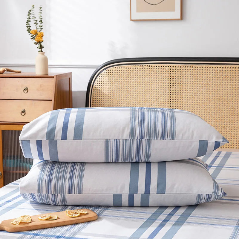 Coussins à rayures bleues et blanches posés sur un lit avec un vase de fleurs et un petit présentoir en bois sur une commode en bois.