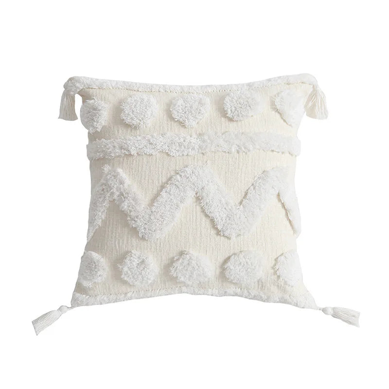 Coussin décoratif blanc moelleux avec des pompons et des glands.