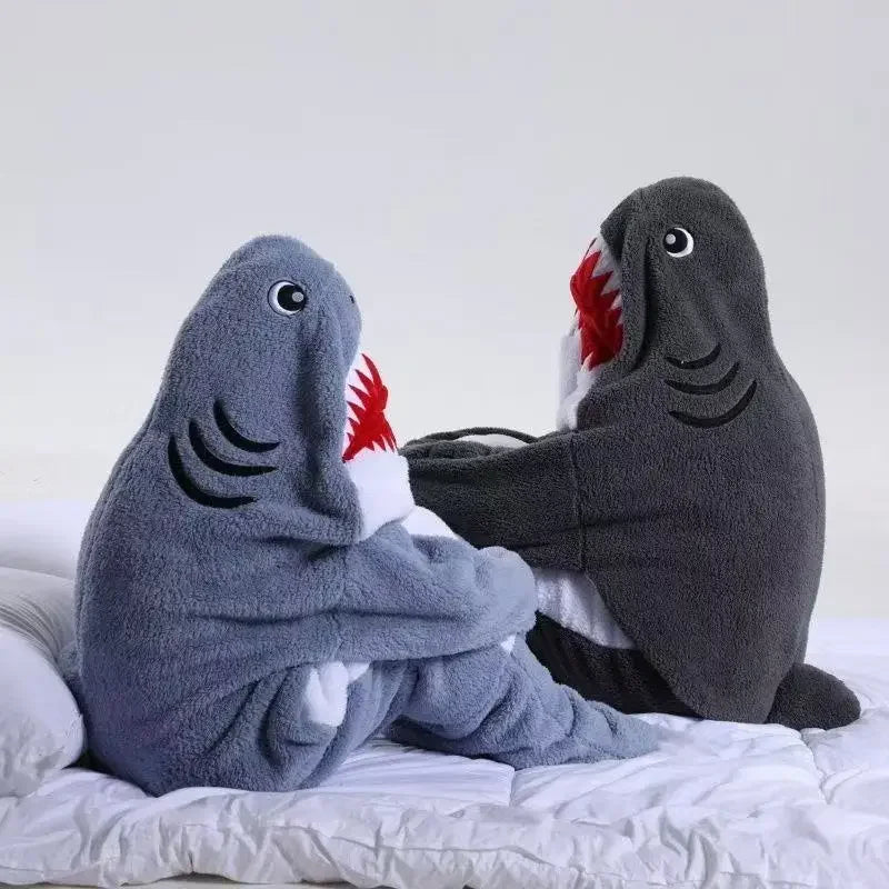 Deux peluches de requins gris posés sur un lit blanc avec des yeux et des dents rouges.