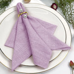 Une serviette de table violette ornée de perles dorées repose sur une assiette blanche entourée de fleurs et de feuillages.