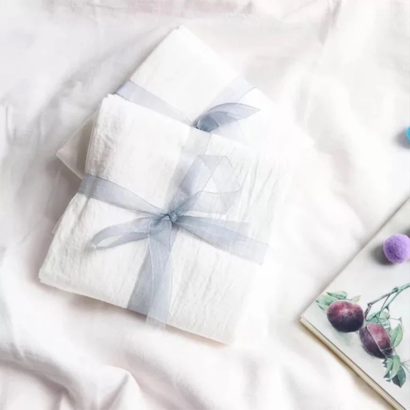Un magnifique cadeau délicatement emballé dans du papier blanc avec un ruban argenté, posé sur une couverture blanche avec quelques décorations florales.