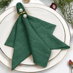 Un magnifique pli de serviette en tissu vert foncé, orné de perles blanches et entouré de fleurs décoratives sur un plateau blanc.