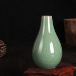 Un vase en verre de couleur vert clair, à la forme élégante et arrondie, posé sur une surface sombre et texturée.