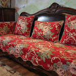 Canapé vintage en bois foncé avec un motif floral rouge, vert et beige sur les coussins, créant une atmosphère élégante et chaleureuse dans la pièce.