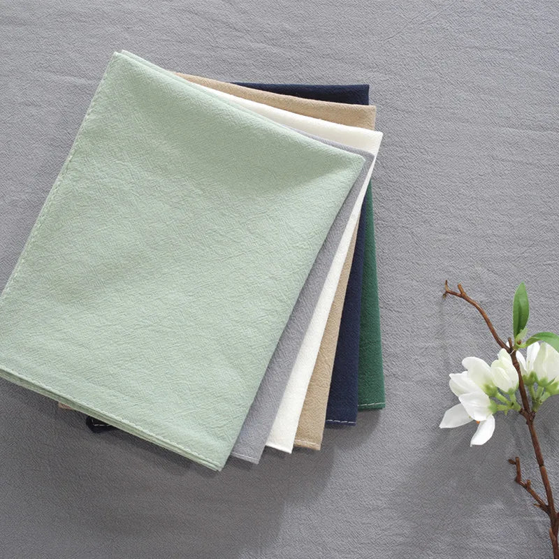 Pile de serviettes en tissu colorées près d'une branche avec des fleurs blanches sur un fond gris.