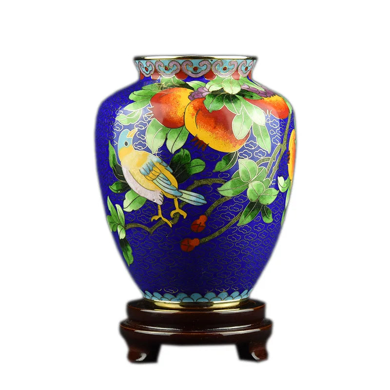 Un vase en céramique émaillée aux motifs floraux et d'oiseaux sur un fond bleu profond, sur un socle en bois.