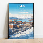 Cette image illustre une vue panoramique de la ville d'Oslo, en Norvège, sous la neige. On peut y voir le paysage urbain enneigé avec ses bâtiments caractéristiques, surplombant un fjord bleu sous un ciel dégagé.