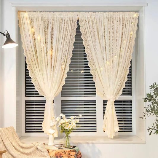 Voilage beige à motif dentelle installé sur une fenêtre à stores horizontaux, agrémenté d'une guirlande lumineuse, dans un intérieur chaleureux avec bouquet de marguerites.