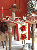 Une table de Noël richement décorée avec une nappe à carreaux, des bougies, une fleur de poinsettia dans un vase, et un chat gris endormi au premier plan, dans une atmosphère chaleureuse et festive.