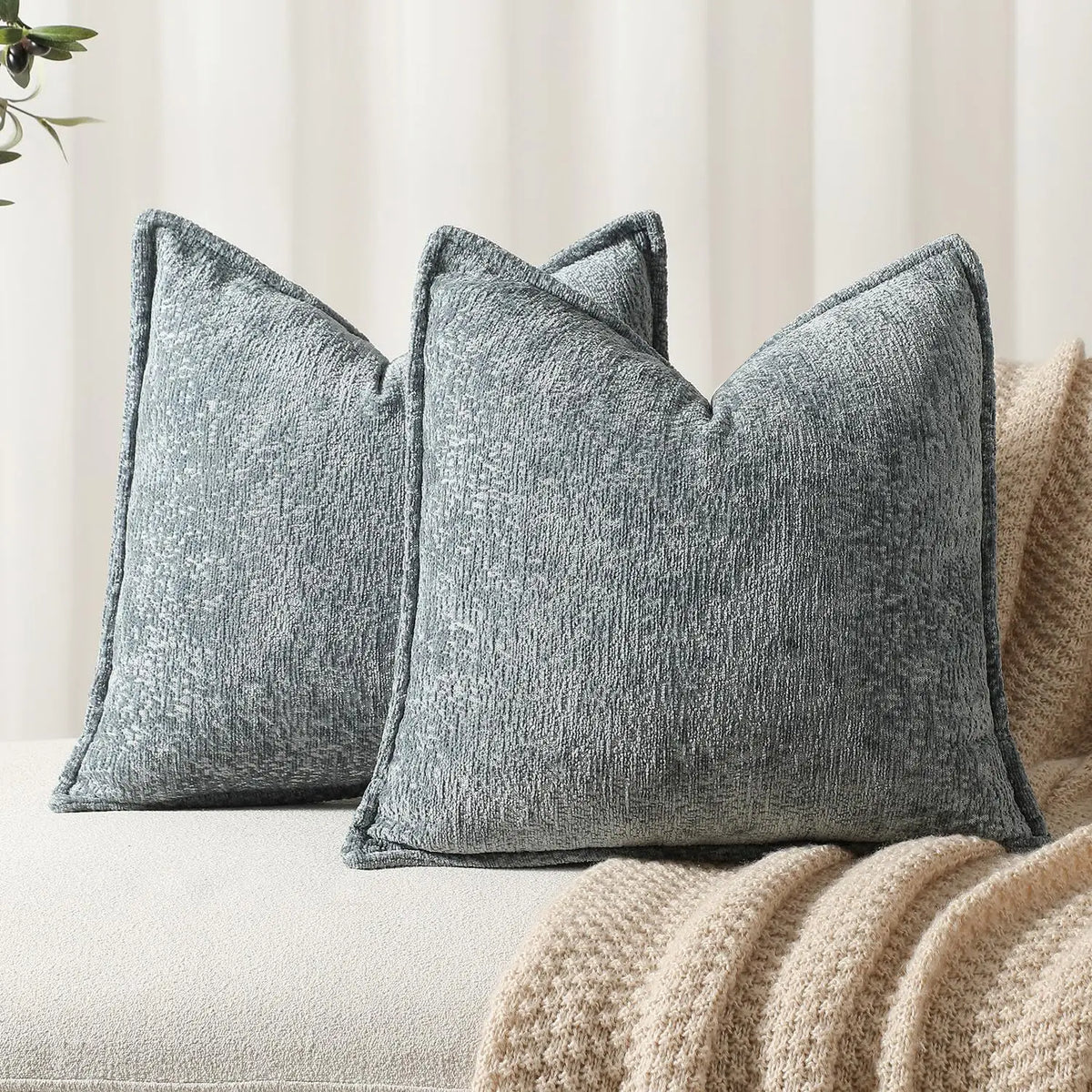 Des coussins décoratifs gris texturés sont disposés sur un canapé, accompagnés d'une couverture beige moelleuse, créant une ambiance confortable et chaleureuse.
