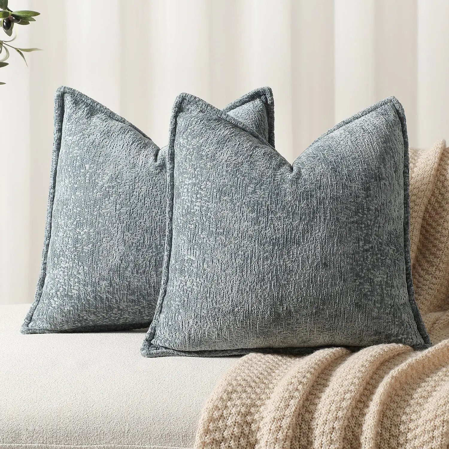 Des coussins décoratifs gris texturés sont disposés sur un canapé, accompagnés d'une couverture beige moelleuse, créant une ambiance confortable et chaleureuse.