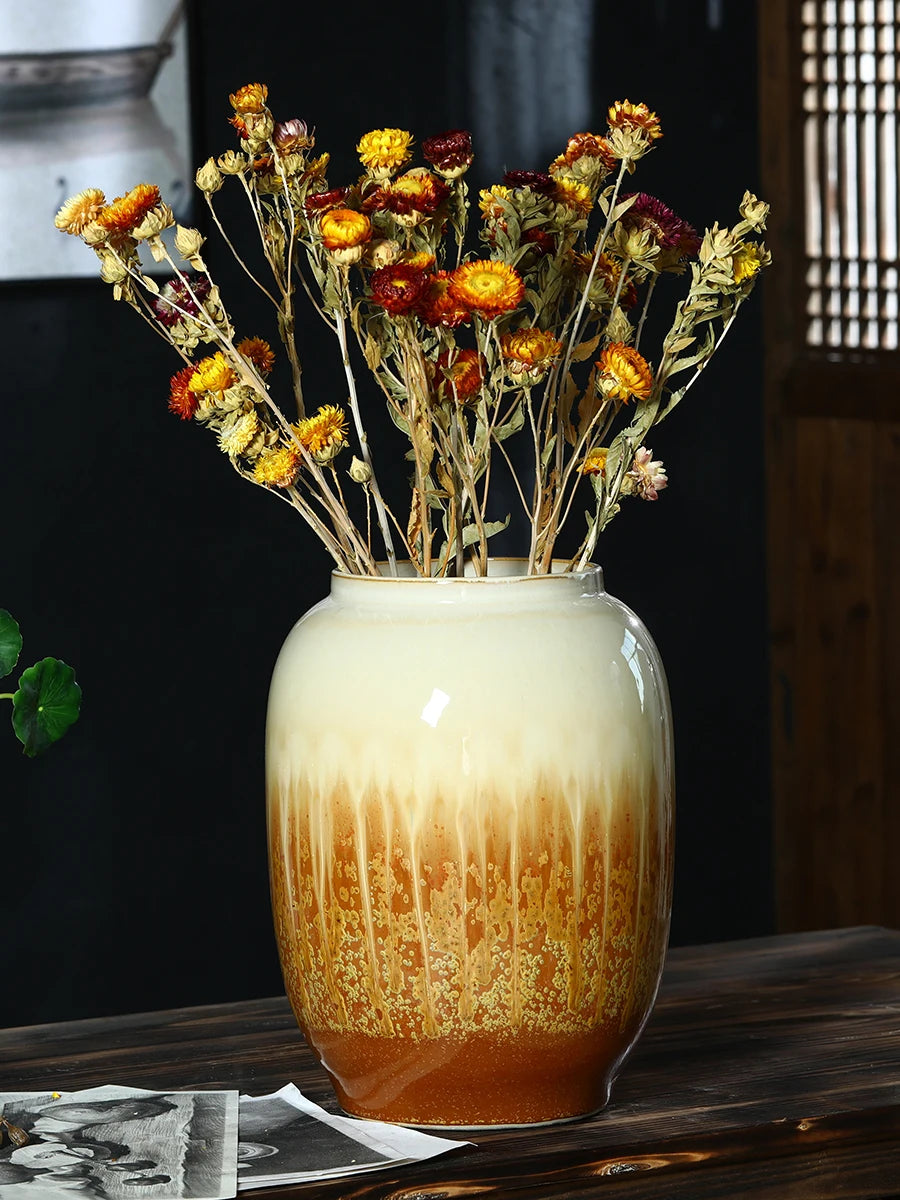 Bouquet de fleurs d'automne séchées dans un vase en céramique décoré d'un fini crème et doré, entouré de vieilles photos sur un fond sombre.