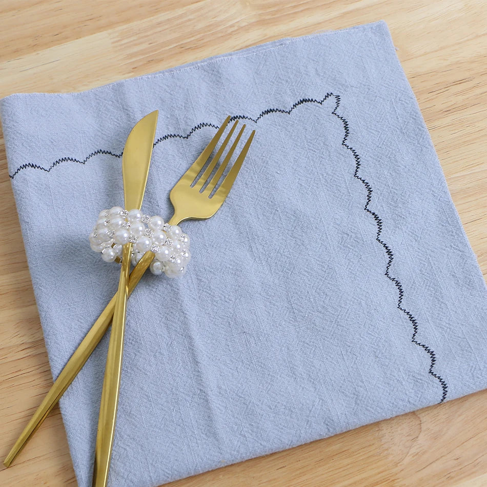 Une élégante serviette grise ornée d'un accoutrement doré et perlé, prête à agrémenter une table de fête.