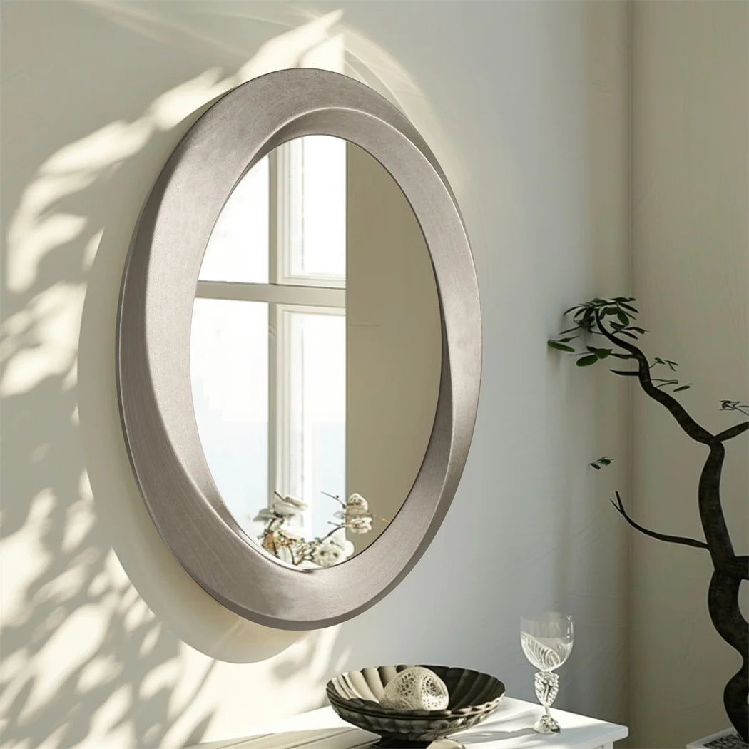 Miroir ovale moderne à cadre en métal argenté dans un intérieur lumineux avec une plante d'ornement.