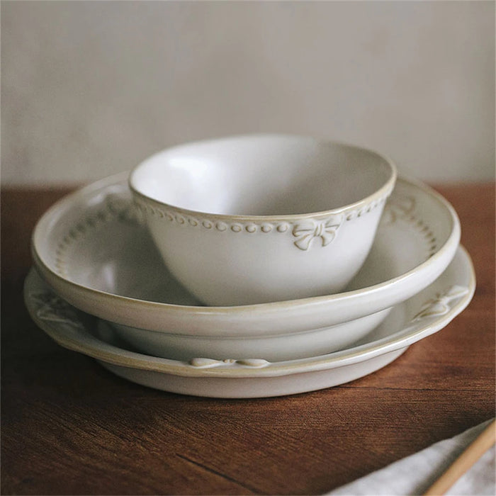 Une pile de bols et assiettes en porcelaine blanche décorée d'un motif floral élégant, posés sur une table en bois sombre.