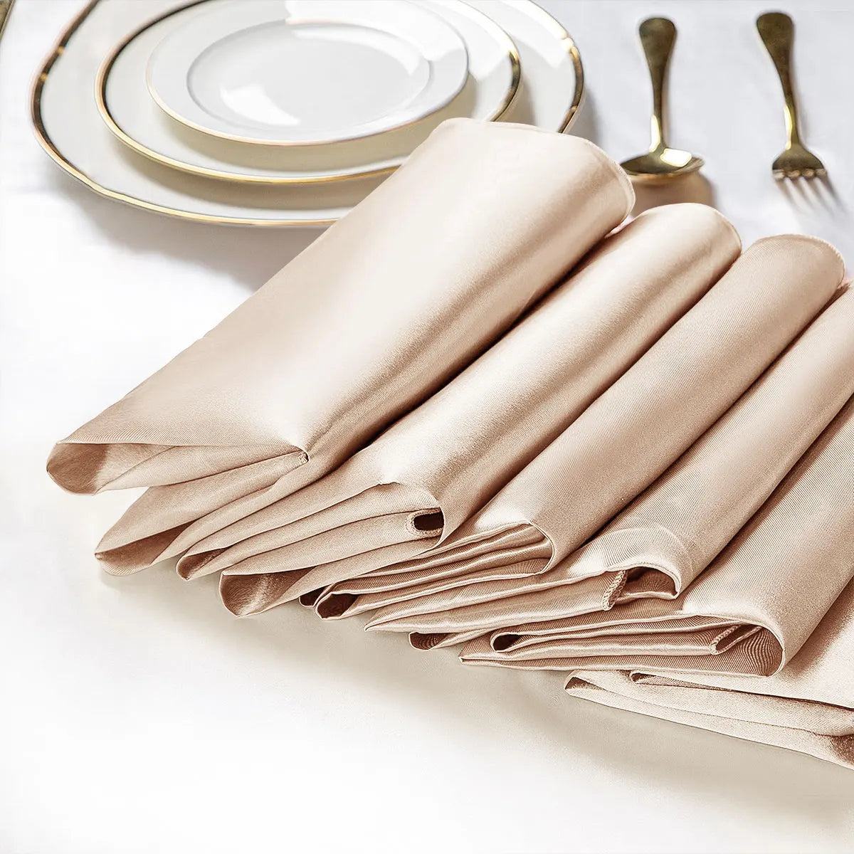 Des serviettes de table en lin beige, pliées avec élégance, sont disposées à côté d'assiettes et de couverts dorés, créant une table de fête sophistiquée.