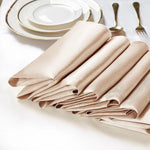 Des serviettes de table en lin beige, pliées avec élégance, sont disposées à côté d'assiettes et de couverts dorés, créant une table de fête sophistiquée.