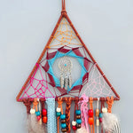 Une captivante décoration murale colorée en forme de triangle suspendue par des cordes, ornée d'un attrapeur de rêves et de perles multicolores.