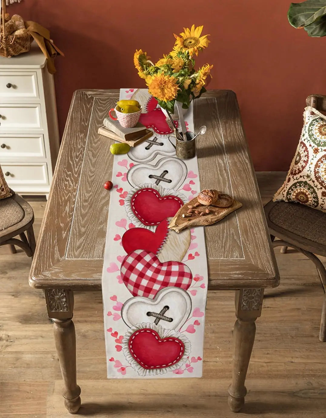 Une décoration de table romantique avec des fleurs jaunes, une nappe aux motifs de cœurs rouges et des pains rustiques.