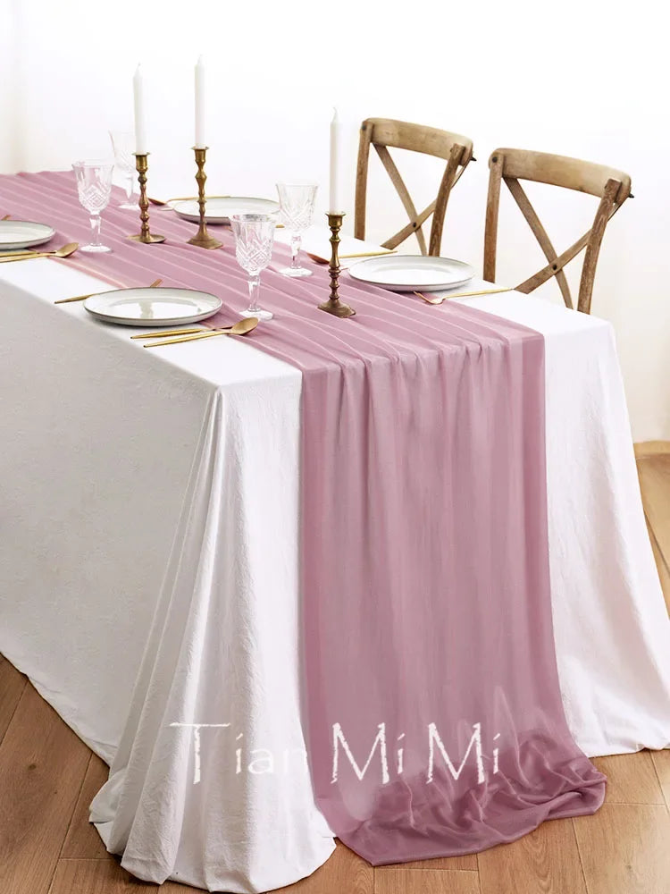 Élégante table de dîner avec nappes roses, bougeoirs dorés et chaises en bois dans un environnement lumineux et épuré.