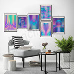 L'image montre une décoration murale composée de plusieurs affiches géométriques et psychédéliques dans des teintes de bleu, de violet et de rose, surplombant un coin salon avec un fauteuil gris rayé, une table basse et des éléments décoratifs.