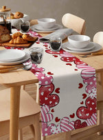 Une table à manger avec de belles assiettes blanches et des bols, un chemin de table avec des motifs cœurs rouges et roses, ainsi que des viennoiseries et des boissons sur la surface en bois.