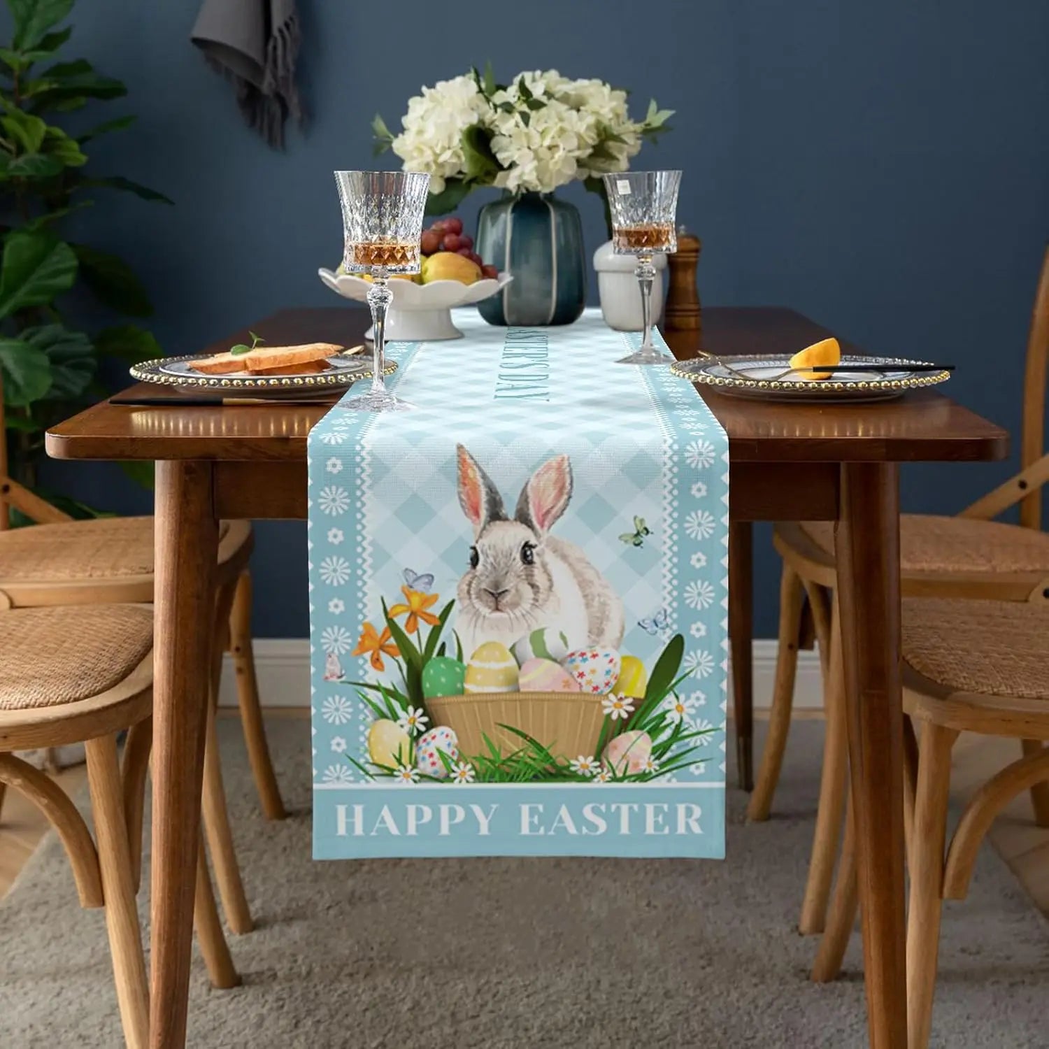 Une décoration de table de Pâques avec un chemin de table orné d'un lapin et de fleurs, accompagné de verres à vin et de fruits, créant une ambiance chaleureuse et festive.