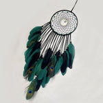 Un magnifique attrape-rêves circulaire garni de plumes de paon vert foncé et de plumes noires, formant une belle composition décorative.