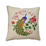 Un coussin décoratif avec un beau motif brodé représentant un paon dans un paysage fleuri.