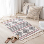 Tapis décoratif géométrique beige et gris avec franges dans un intérieur lumineux.